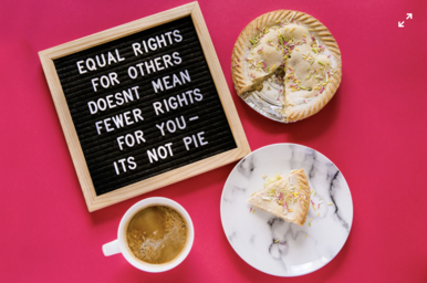 White ceramic plate with pie, coffee in a mug and a sign saying \' equal rights for others doesn\'t mean fewer rights\' on a pink background