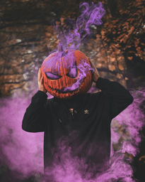 Man with a carved pumpkin on his head surrounded by purple smoke