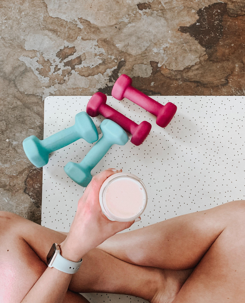 person holding drink in a glass sitting hear dumbbells