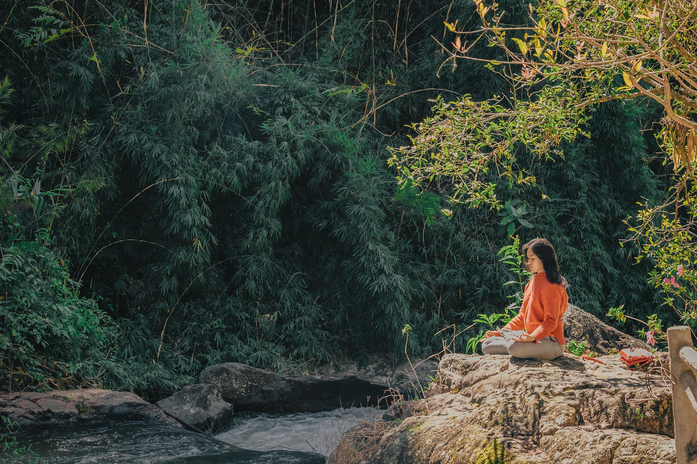 woman meditating on a rock by a river in a forest