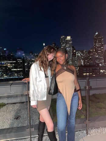 Photo of two girls posing for the camera, with the city night skyline in the background.