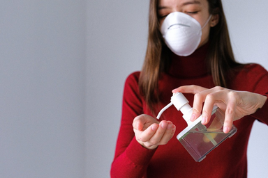 woman wearing mask using hand sanitizer