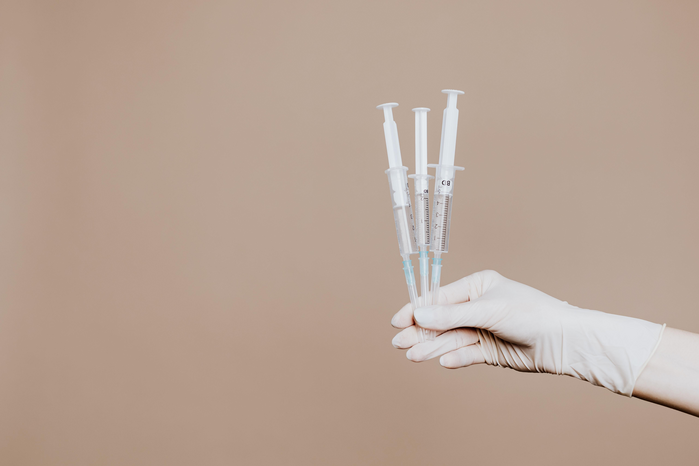 a medical gloved hand holding three syringes by Karolina Grabowska