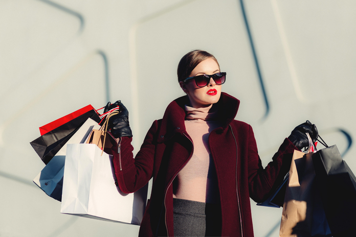 Woman with magenta coat and sunglasses holding up shopping bags