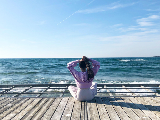 woman sitting on boardwalk facing ocean by Birti Ishar via Unsplash
