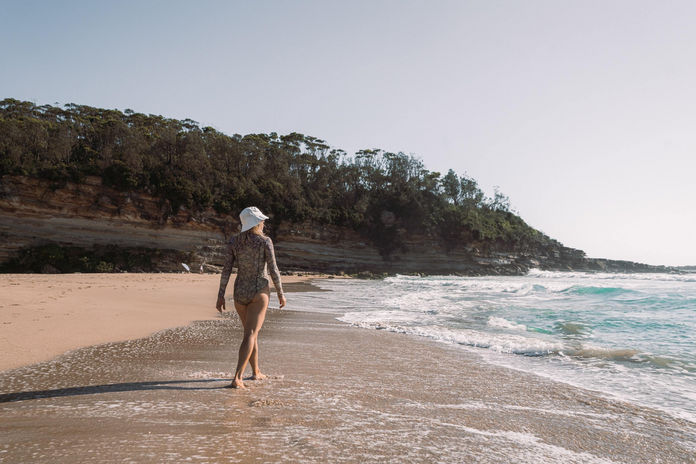 Woman in a long-sleeved body/swim suit walking on the beach.