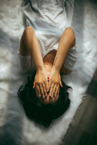 woman laying on bed covering face with hands by Anthony Tran via Unsplash