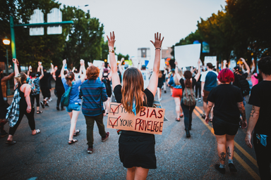 people walking at a protest, focus on one woman that has a sign on her back and her hands up