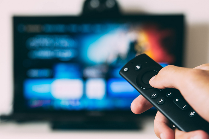 person holding remote pointing at tv by Glenn Carstens Peters via Unsplash
