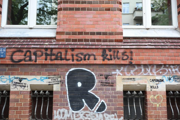 brown brick building \"capitalism kills!\" graffiti