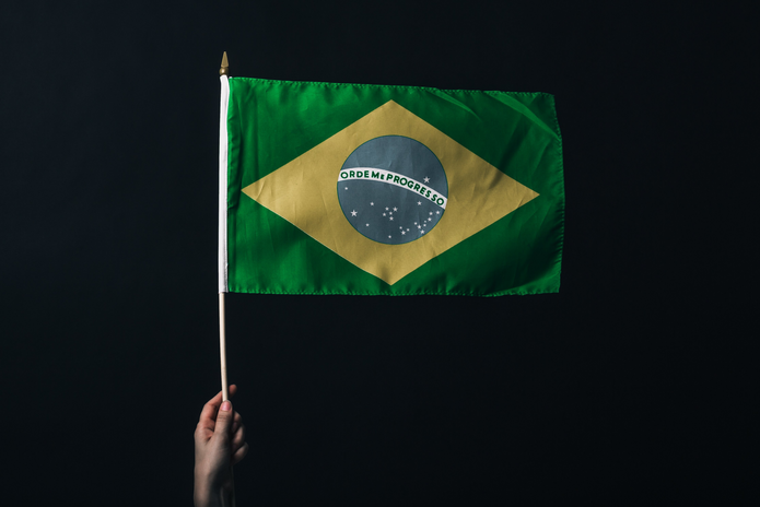 Brazilian flag being held by a hand against a black back drop