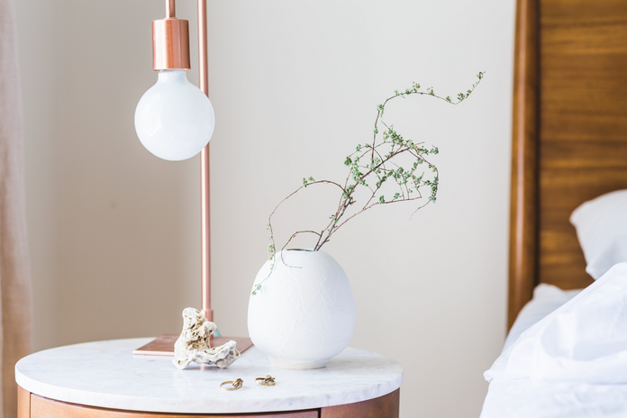 white and rose gold bedside table lamp next to bed with plant