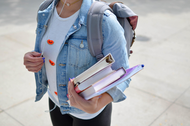 Student walking with books in hand while wearing headphones