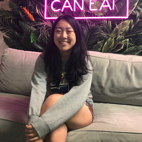 Photo of Chloe Boscov-Brown sitting on a white couch in front of a neon sign.