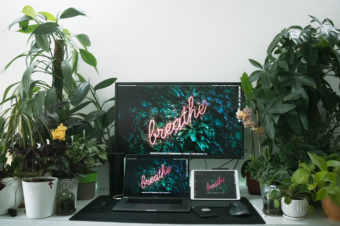 Neon pink breathe sign on computer surrounded by plants