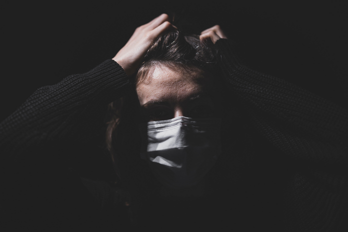 Woman wearing a mask holding her head against a black background.