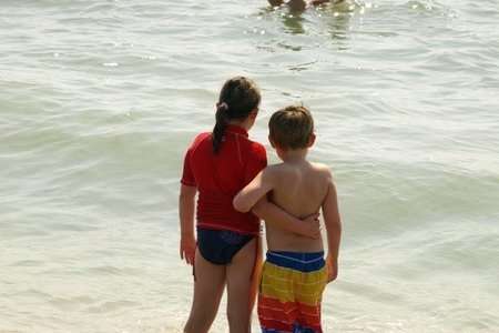 A little boy and girl with arms around each other at the beach