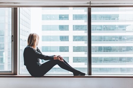 Woman sitting on a white window sill looking out into the distance