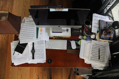 Messy desk with a computer and sheet music