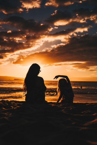 mother and daughter sitting on the beach in front of a sunset
