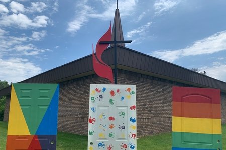 Rainbow painted doors in front of metal cross