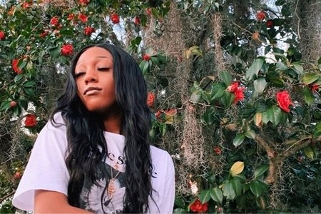 Girl in a white shirt in front of an ivy and roses-covered wall