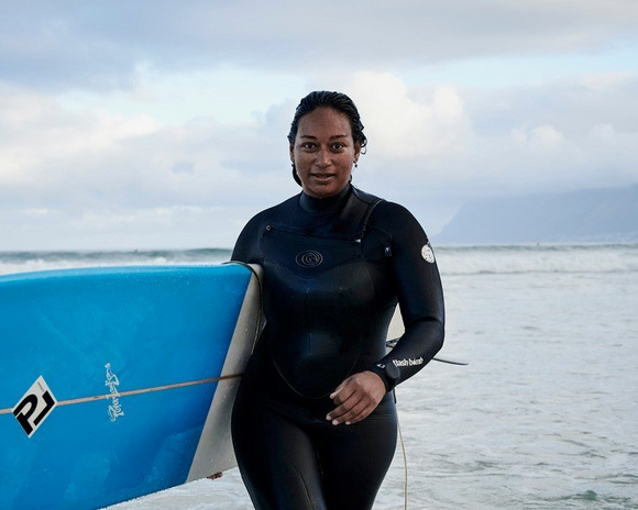 Aaniyah Omardien walking out of the sea with her surfboard.