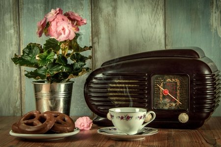 antique radio, pink flowers, pretzels, and tea cup on a wooden table with blue worn wood backdrop