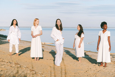five women in all white standing on the beach