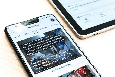 silver iphone 6 on brown wooden table with news feed on screen
