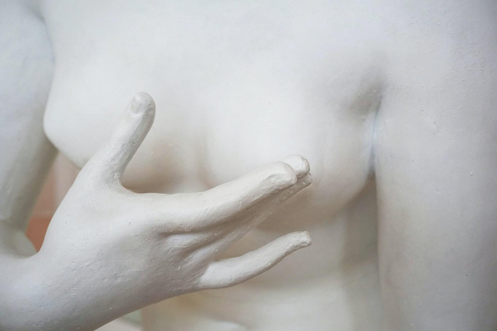 A marble statue of a person touching their left breast.
