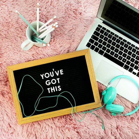 A board with \"You\'ve got this\" next to blue headphones, a laptop, and a pencil stand