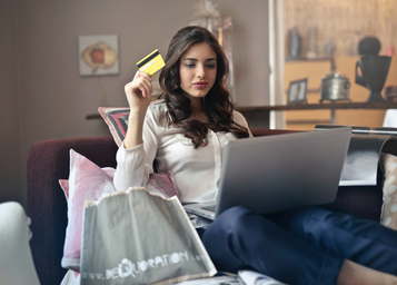 Woman holding a credit card in front of a laptop with shopping bags beside her.