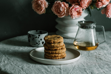 cookies stacked on a plate with table cloth and flowers in background