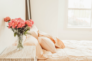 four orange pillows on a bed with flowers on the bedside table