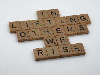 scrabble letters on a white table that spell out \"in lifting others we rise\"
