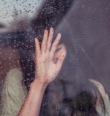 A woman presses her hand against a rainy glass window