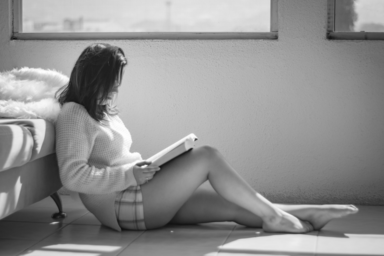black and white photo of a woman sitting on the floor reading a book