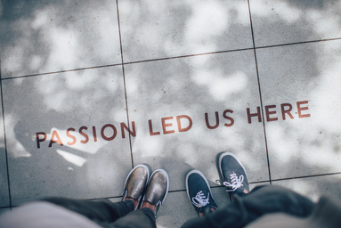 Two people standing on paved gray tiles that read, \"Passion led us here.\"