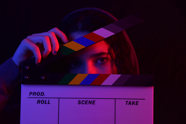 Woman holding a colorful clapperboard in a dark background