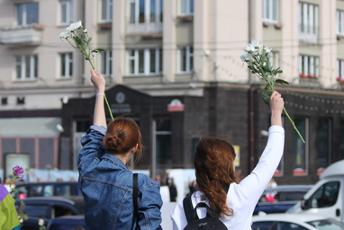 Two girls holding up flowers on a street corner