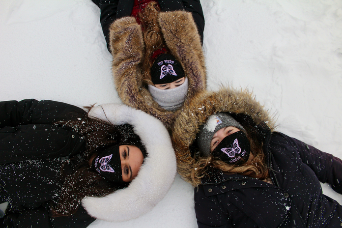 Three women laying in the snow on campus