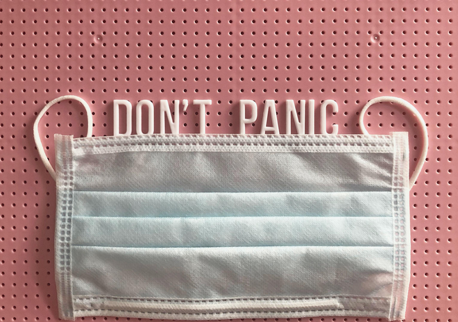 mask on a pink letterboard with the words "don't panic" written