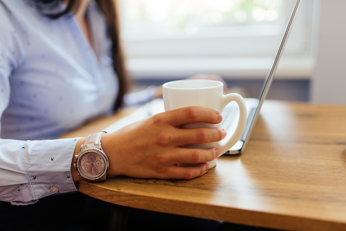 Woman wearing watch holding coffee mug while at laptop
