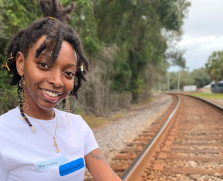 owner of Erevu Styles wearing a white shirt next to a train track.