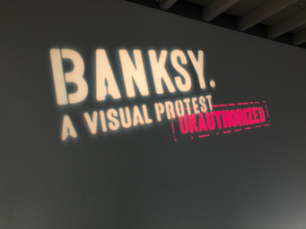 The name of the exhibition \"Banksy. A Visual Protest\" held in a Finnish museum called Art Museum Gösta. Title projected on the gallery wall.
