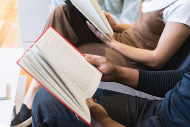 Two people read books together on a couch
