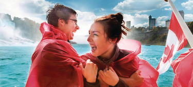 Two people laugh while wearing red ponchos in front of Niagara Falls