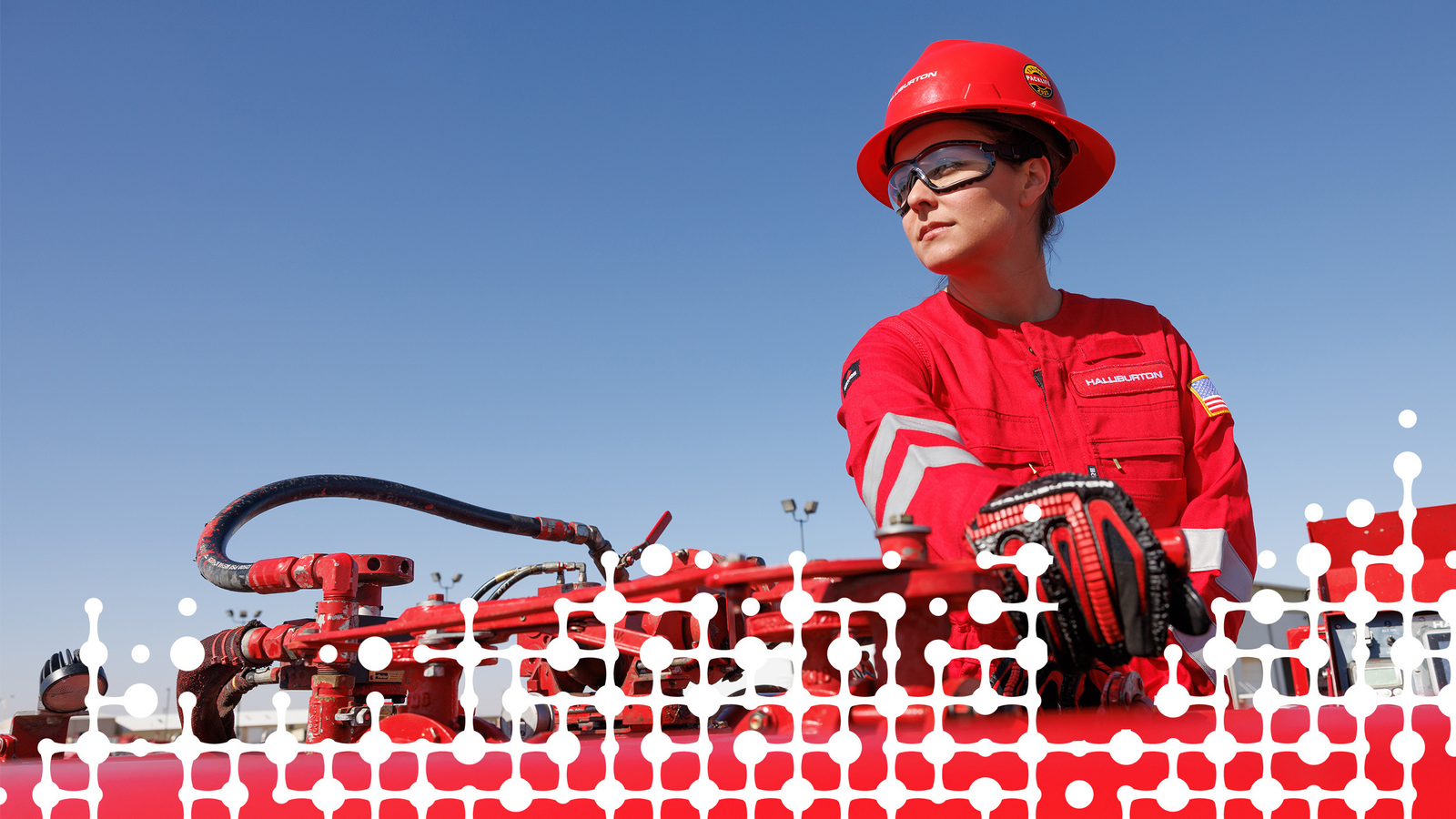 Halliburton employee in a hard hat stands in front of industrial equipment with a hose and various valves.